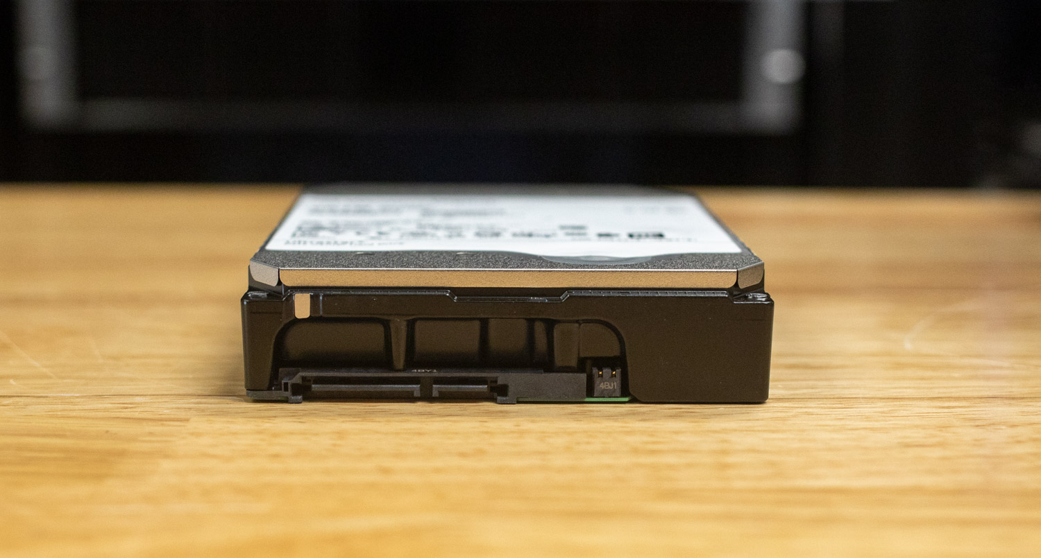 Close-up of the connector side of a Western Digital Ultrastar DC HC590 26TB hard drive resting flat on a wooden surface. The SATA power and data connectors are visible.