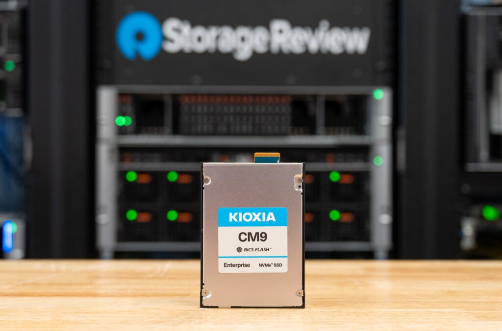 KIOXIA CM9-R 15.36TB E3.S SSD standing upright on the StorageReview lab bench with the drive rack behind it