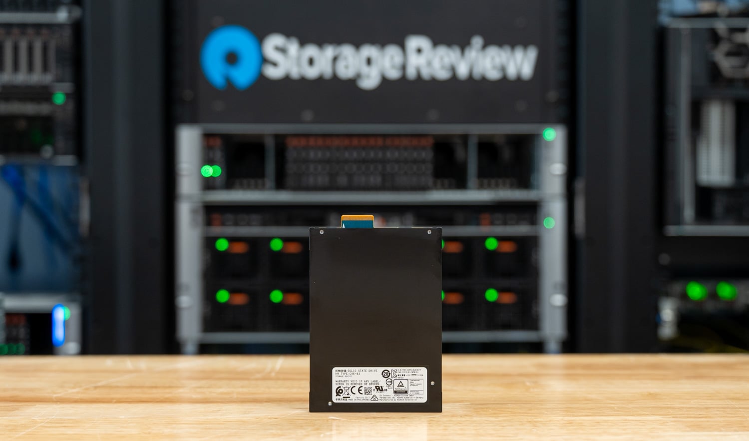 Rear label side of the KIOXIA CM9-R E3.S SSD standing on the StorageReview bench in front of the lab rack