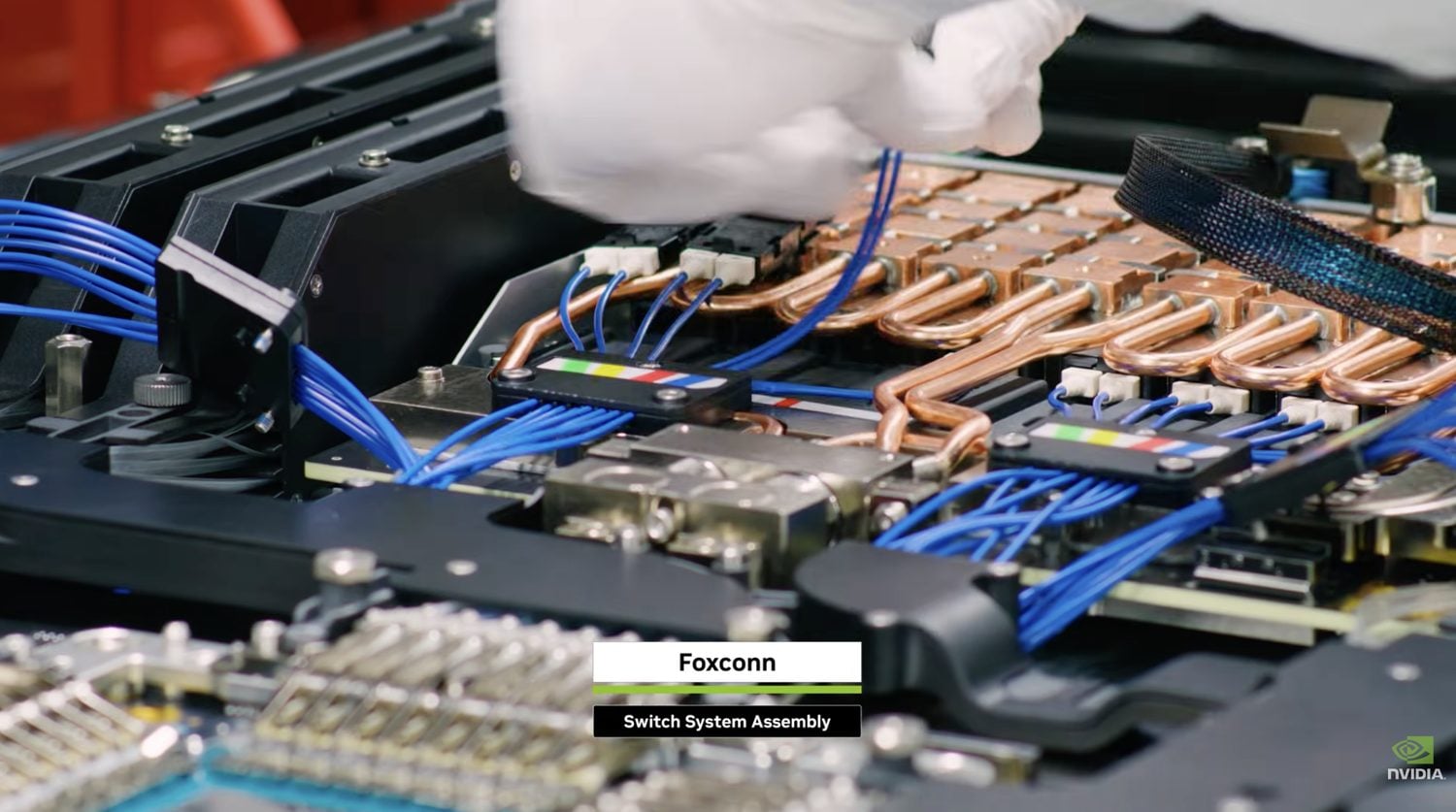 Inside a liquid-cooled NVIDIA Spectrum-X Ethernet Photonics switch during Foxconn assembly, showing copper cooling loops and blue fiber runs