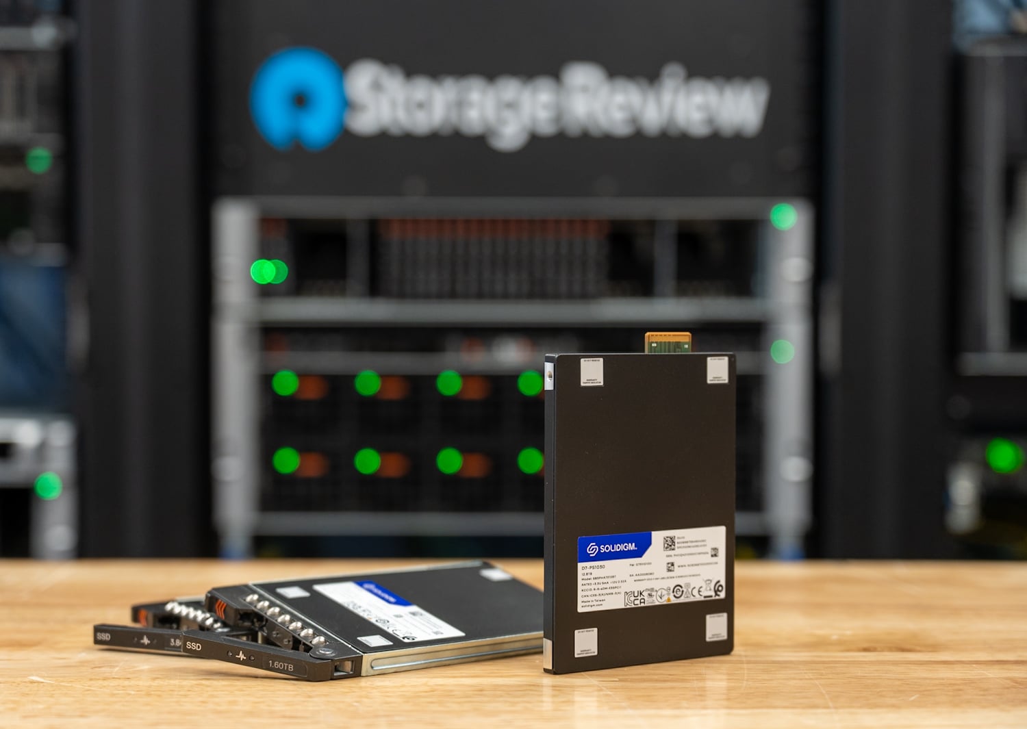 Two Solidigm D7-PS1030 drives, one mounted in an E3.S sled, in front of the StorageReview server rack