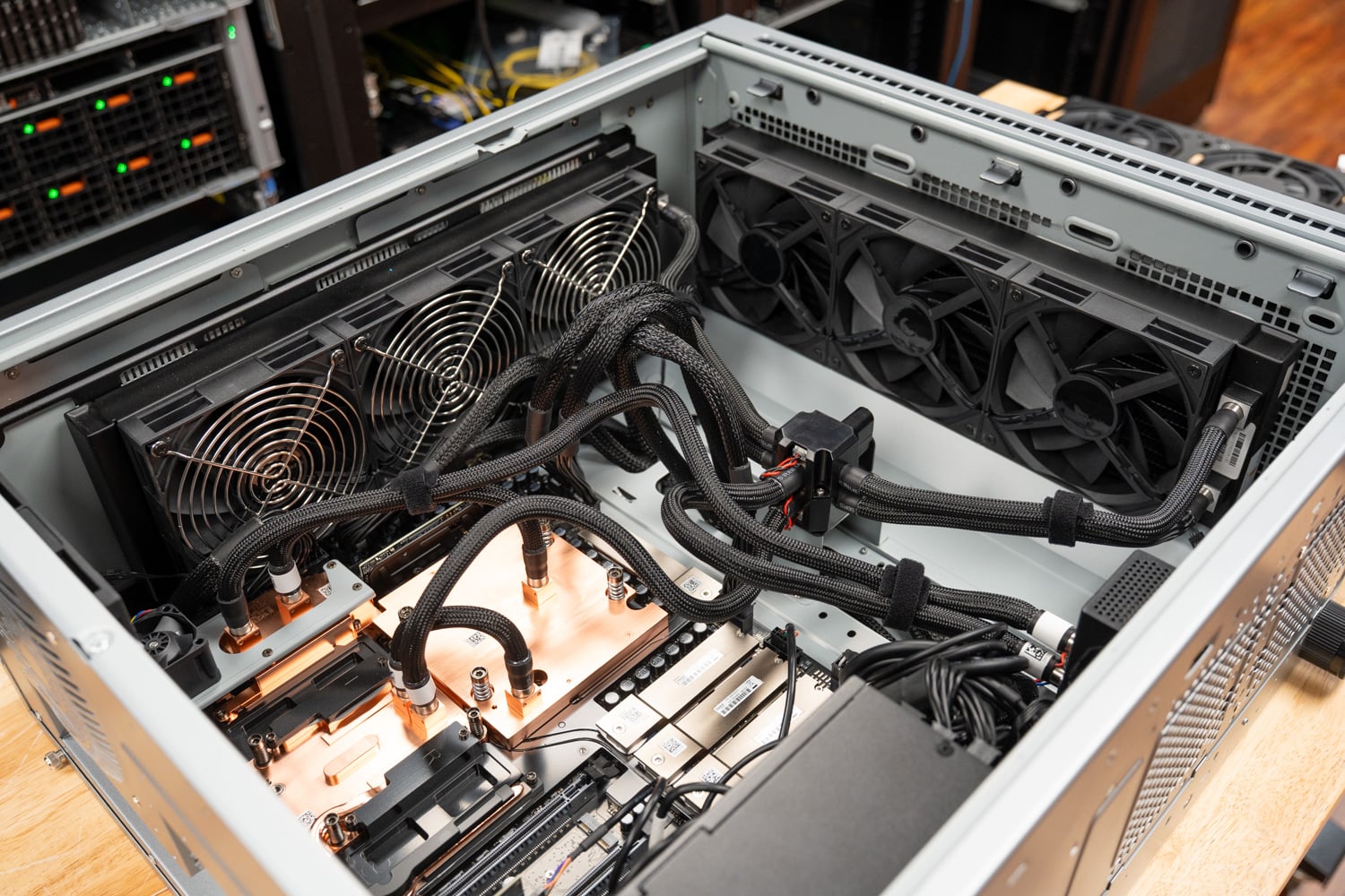 Top-down view into the open ASUS ExpertCenter Pro ET900N G3 in the StorageReview lab, with the three-fan front radiator, the three-fan top radiator, sleeved coolant lines, and the copper cold plates over the GB300 Superchip