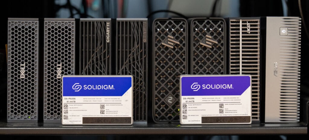 The eight GB10 systems in this DGX Spark shared storage project, two Dell Pro Max with GB10, two GIGABYTE AI TOP ATOM, two HP ZGX Nano G1n, an Acer Veriton GN100, and an ASUS Ascent GX10, lined up on a rack shelf in the StorageReview lab with two Solidigm D5-P5336 61.44TB SSDs in front